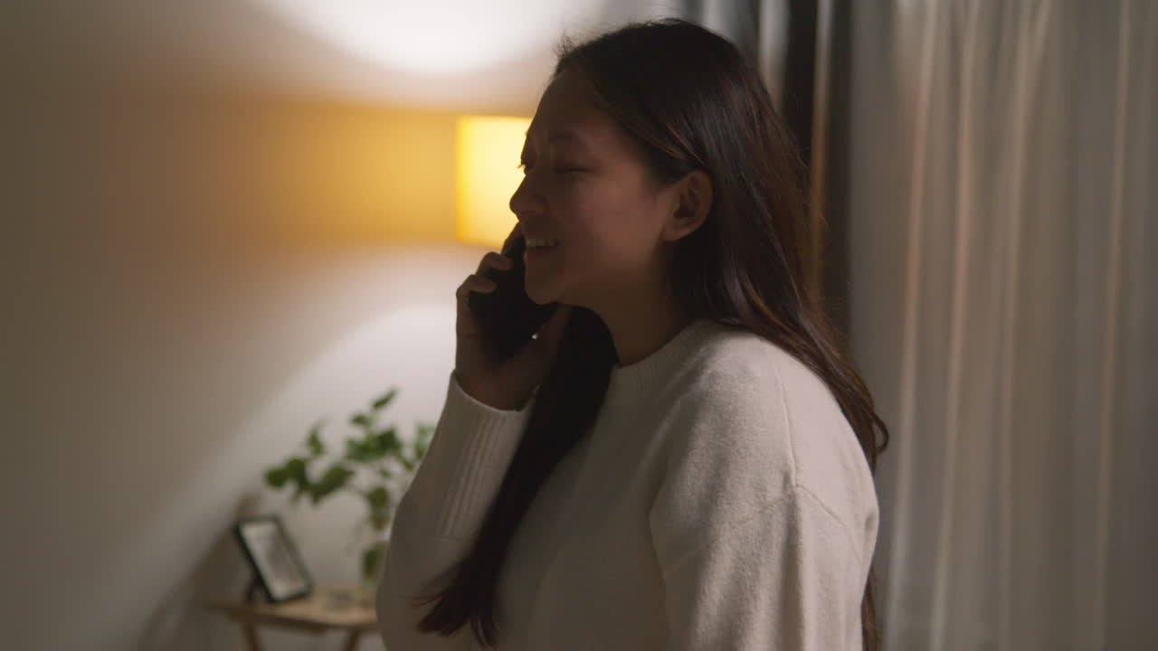 집에서 저녁을 보내는 여성이 휴대 전화로 대화하는 라운지를 돌아다니고 있습니다.