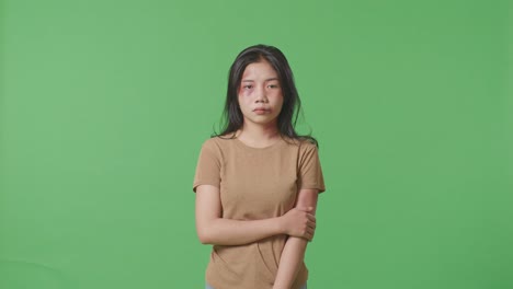 얼굴에 이 있는 폭력의 희생자인 젊은 아시아 여성은 그녀의 팔을 들고 스튜디오의 녹색 스크린 배경에서 슬프게 카메라를 바라보고 있습니다.