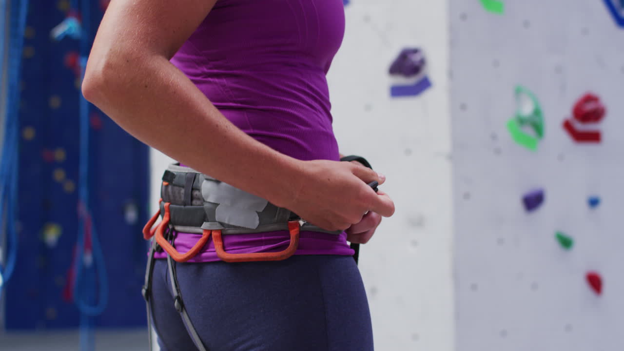 mujer caucásica preparando un cinturón de arnés de escalada para escalar en una pared de escalada interior