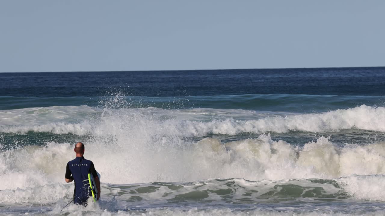 서퍼가 물속으로 들어가서 파도를 마주하고 타고 있습니다.