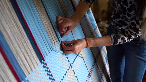 woman weaving blue and beige threads on a vertical loom