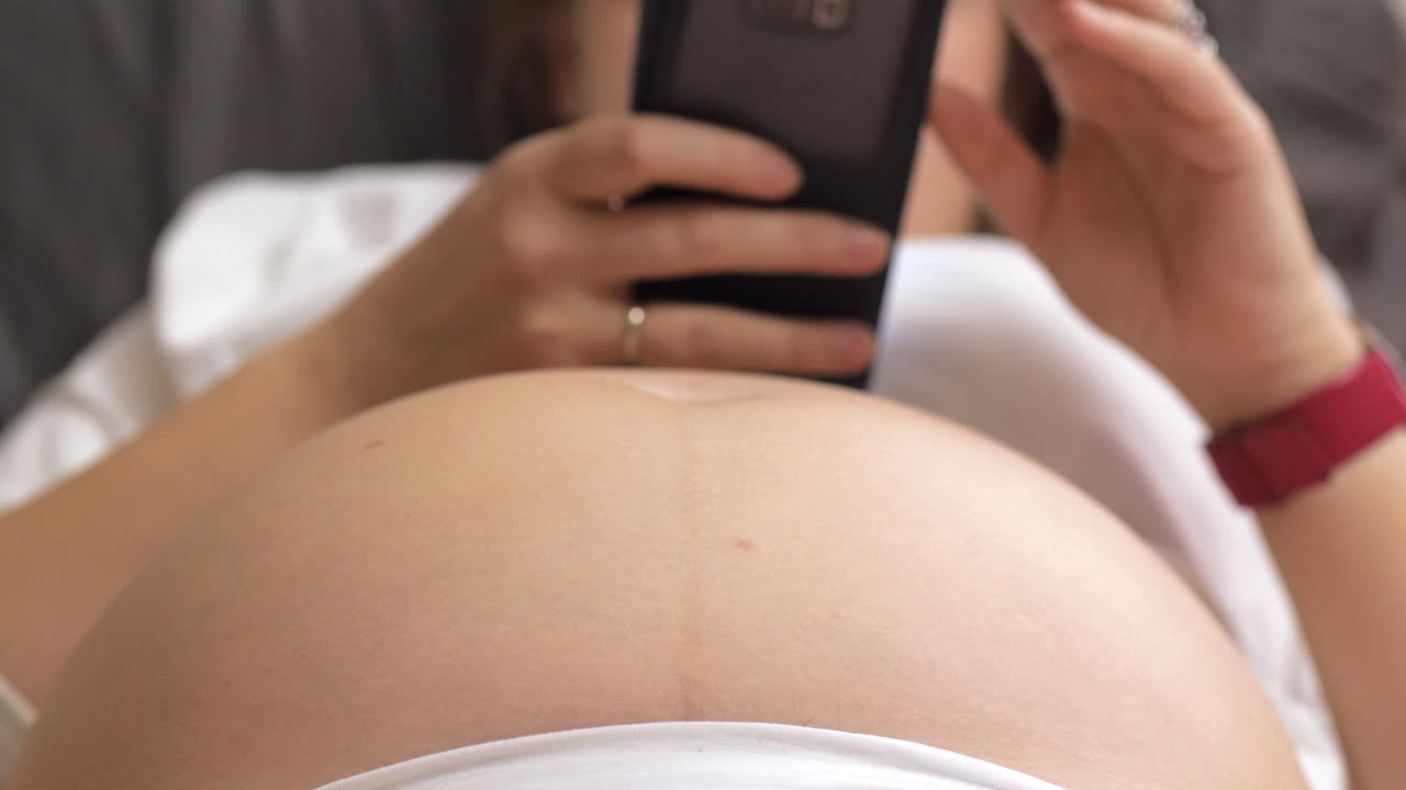 Donna incinta con il cellulare mentre il bambino scalcia nella pancia