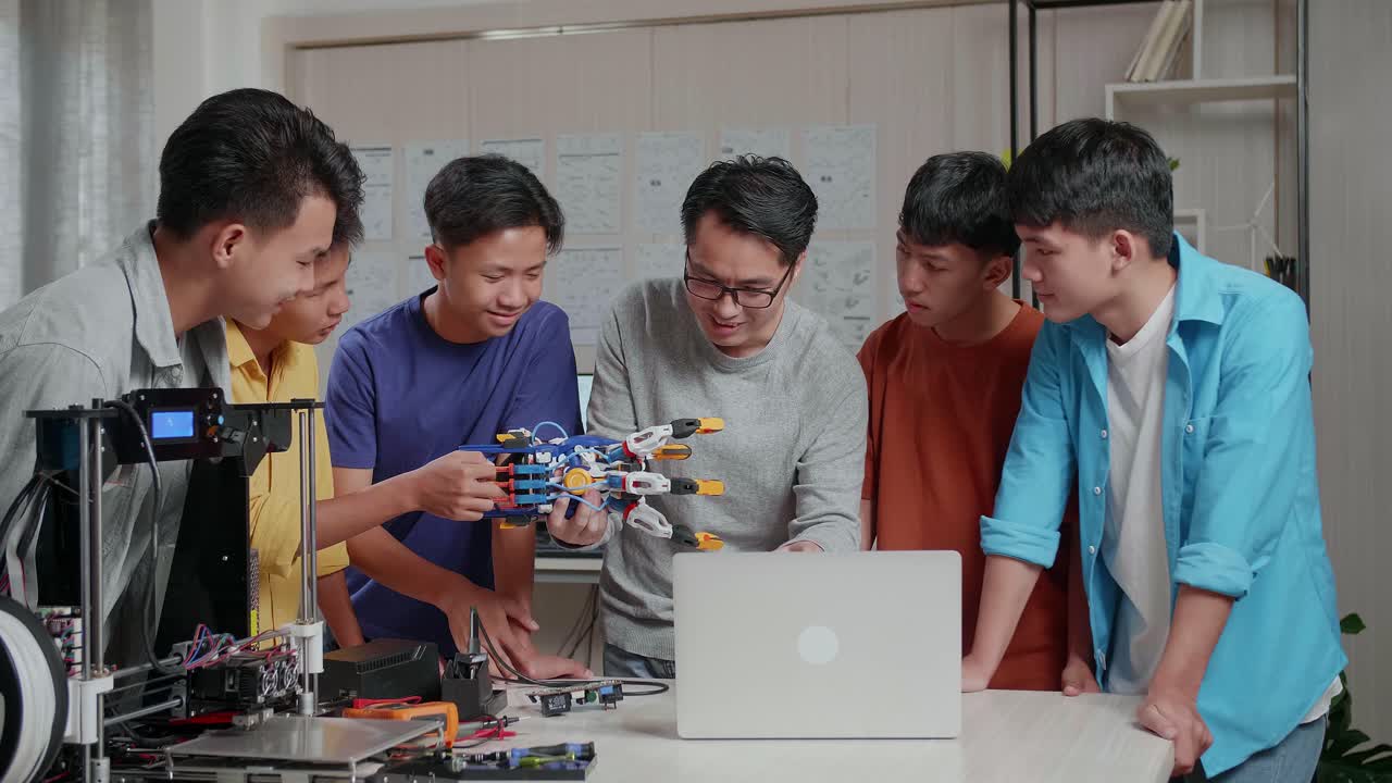 Asian Man With 3D Printing Using A Laptop And Explain About A Cyborg Hand To The Boys At School