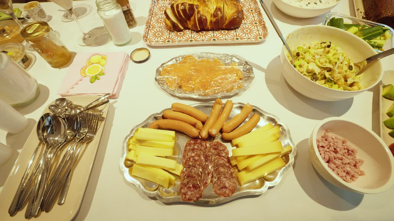 Filmato in stock di alta qualità che mostra mani che dispongono un ricco buffet per la colazione con formaggio, salsicce, affettati, pane e contorni, a simboleggiare ospitalità, cibo fresco, colazione in famiglia e hotel