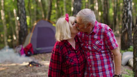 Senior-elderly-grandmother-grandfather-tourists-resting-at-camping-in-wood-over-bonfire-at-camping