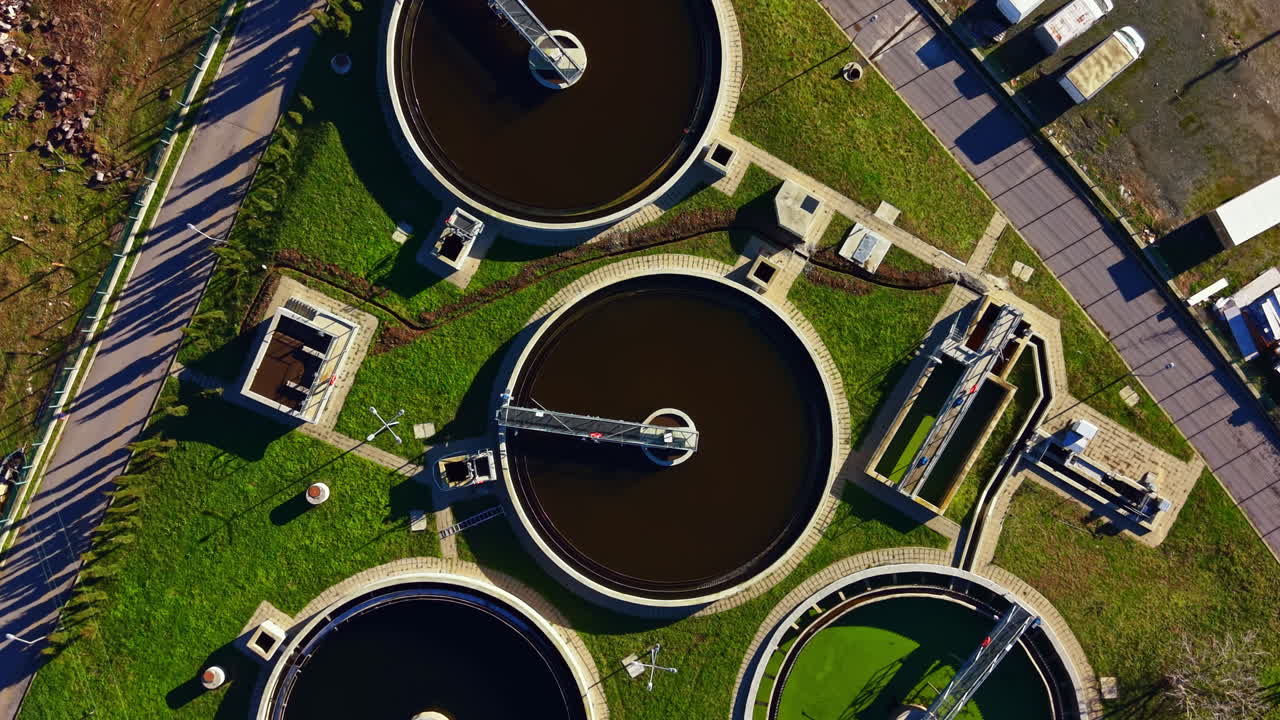 Water treatment facility with large tanks and equipment viewed from above during daytime near city area