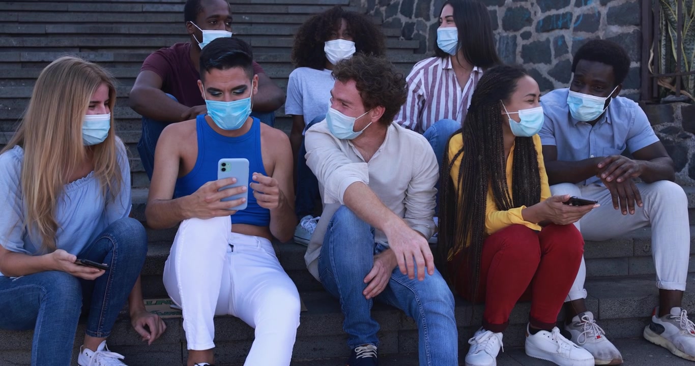 Jóvenes diversos usando mascarillas sentados en escaleras al aire libre