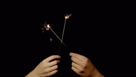 close-up of hands holding and waving bengal fire burning sparklers in front of black background