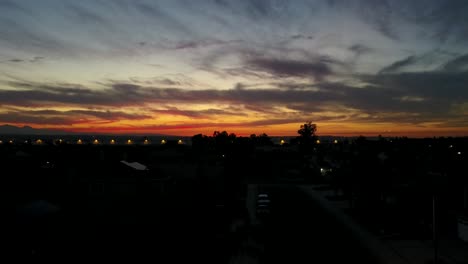 drone rises behind a palm tree to reveal a dark orange sunset with clouds