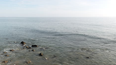 olas tranquilas del océano de la playa de malibu de roca grande con rocas sumergidas en aguas poco profundas