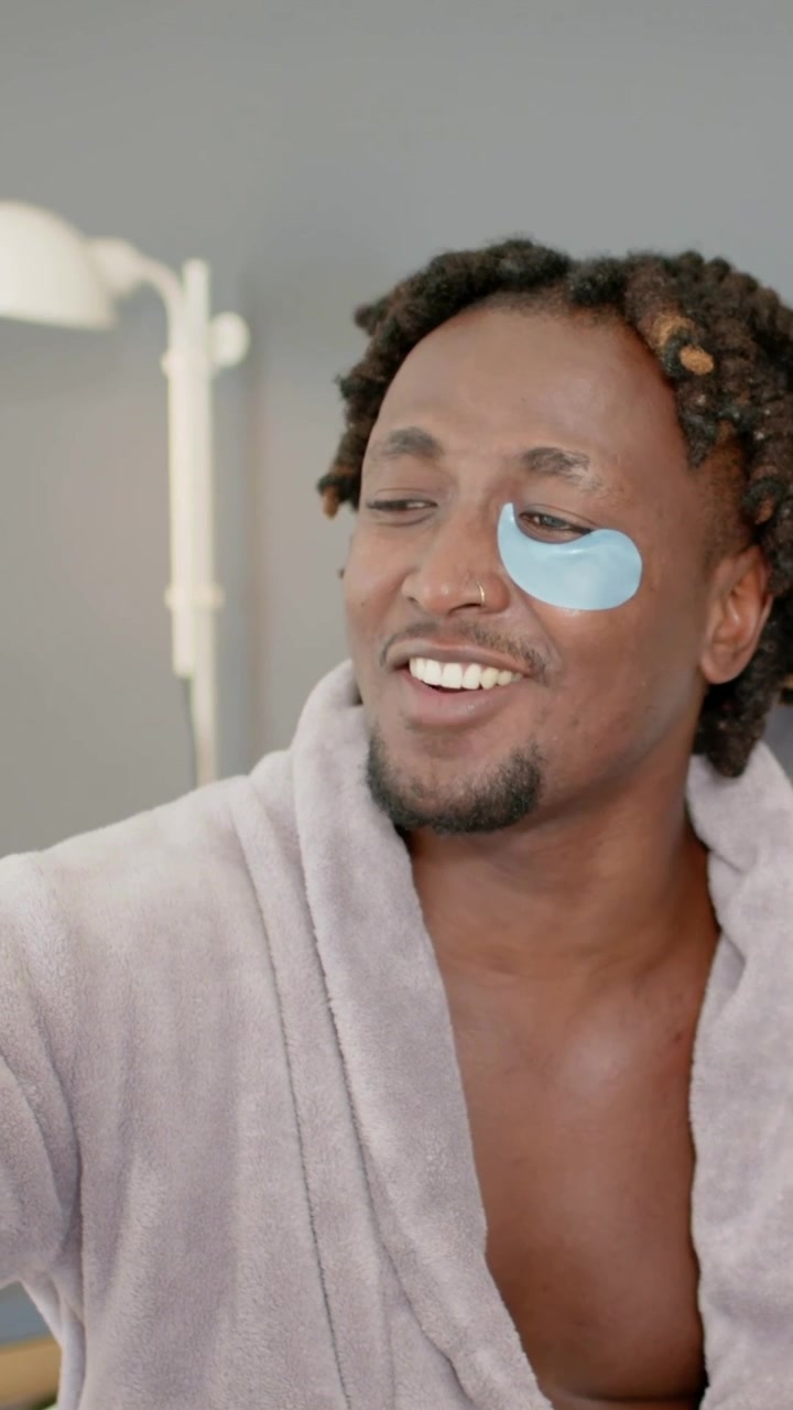 Vertical video: Smiling man in gray robe showing hand to cheer her as entering bed, blue gel patch