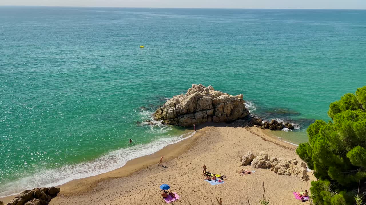 cala roca grossa día soleado de verano turismo europeo mediterráneo paraíso playa vista aérea desde drone contraste con arena de roca y árboles verdes