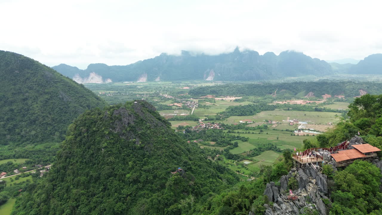 Scenic lookout in Vang Vieng reveals limestone peaks, river curves, and jungle landscape, aerial establishing overview