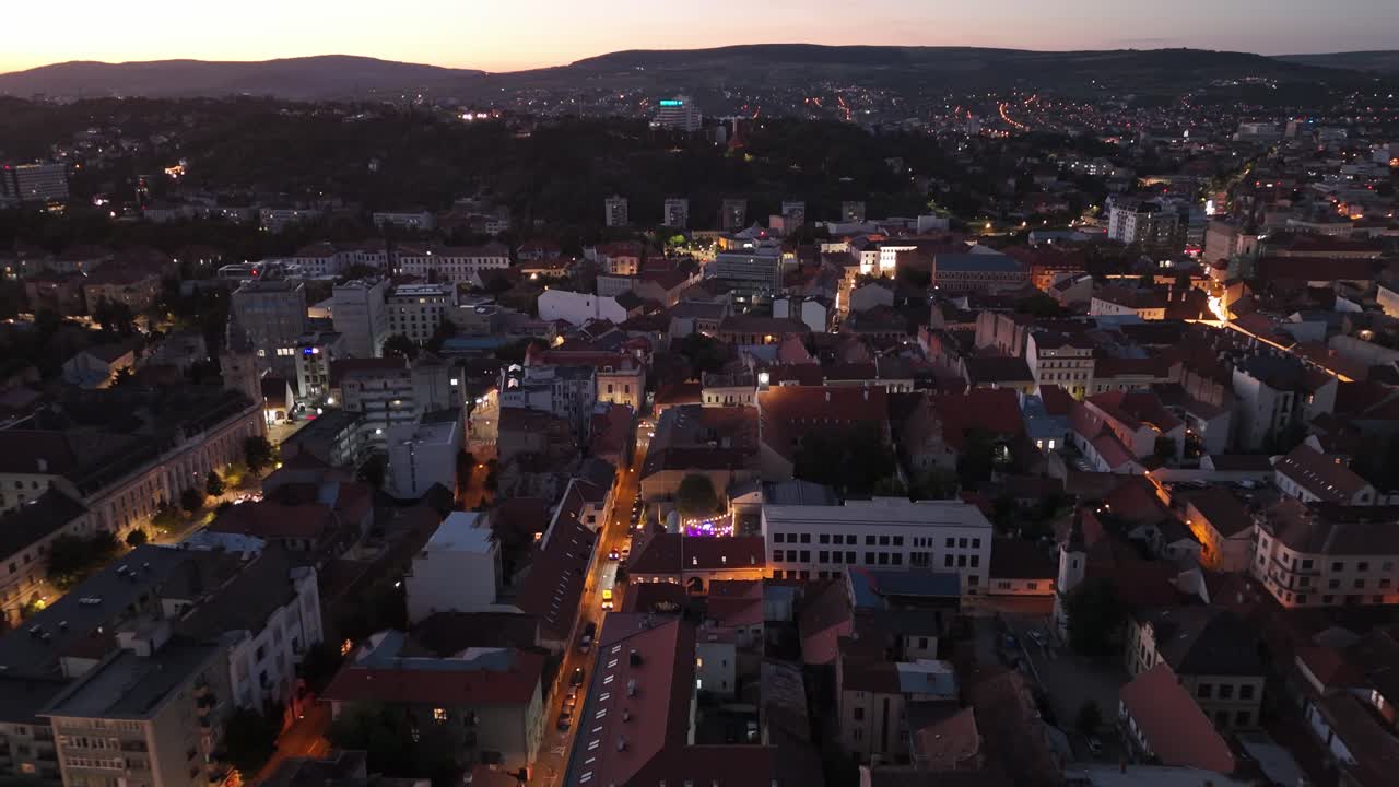 Aerial view of city rooftops at dusk with warm lights and cozy streets