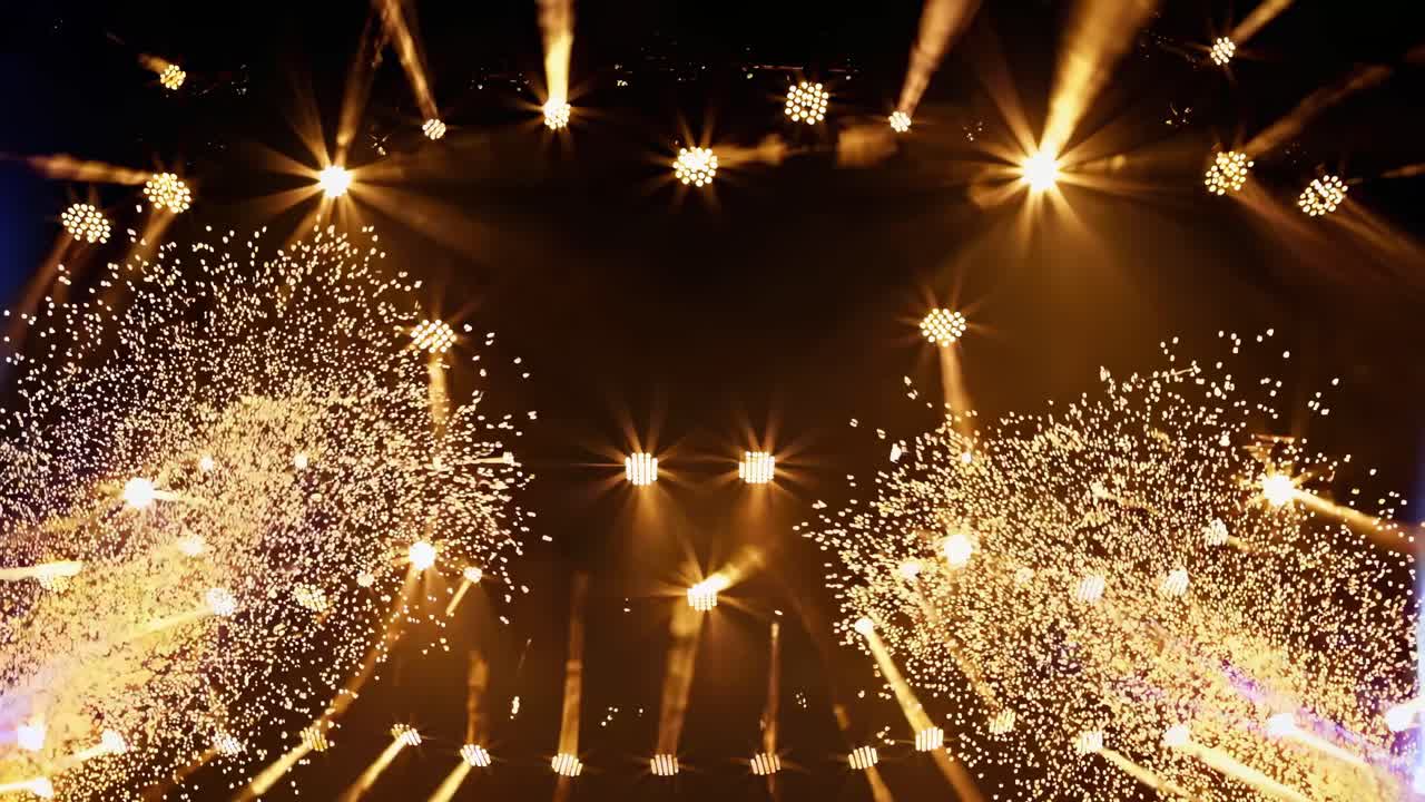 A dynamic video captures a low-angle view of a stage with vibrant blue and gold lights forming