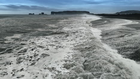 big powerful waves roll on the shore with black sand. dark mountains at backdrop. drone footage above the coastline of iceland.