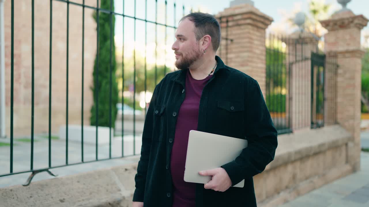 joven de talla plus sonriendo confiado sosteniendo una computadora portátil bailando en la calle