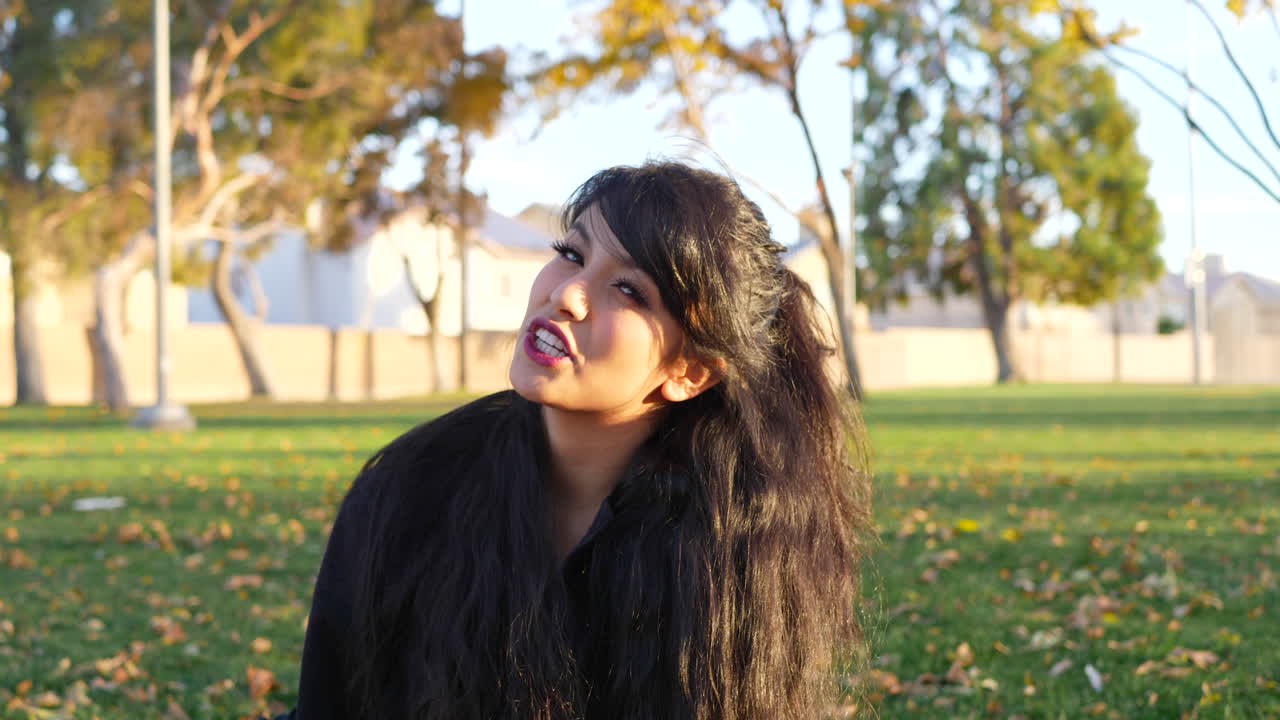 una linda chica sentada en un parque mientras lee un libro electrónico en su tableta lectora de libros electrónicos en cámara lenta rodeada de hojas de otoño
