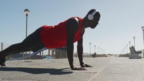 Hombre-Afroamericano-Enfocado-Haciendo-Flexiones,-Haciendo-Ejercicio-Al-Aire-Libre-Junto-Al-Mar