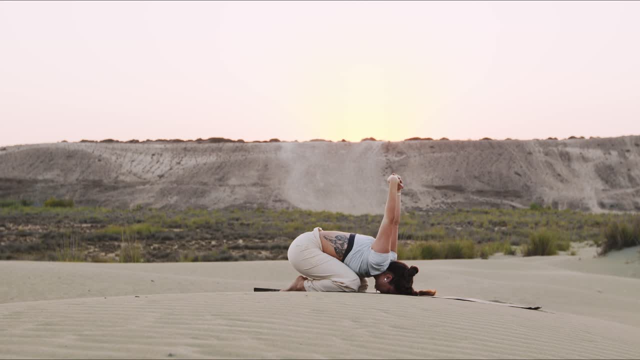 joven instructor de yoga en una colina de arena haciendo una rutina matutina durante el amanecer