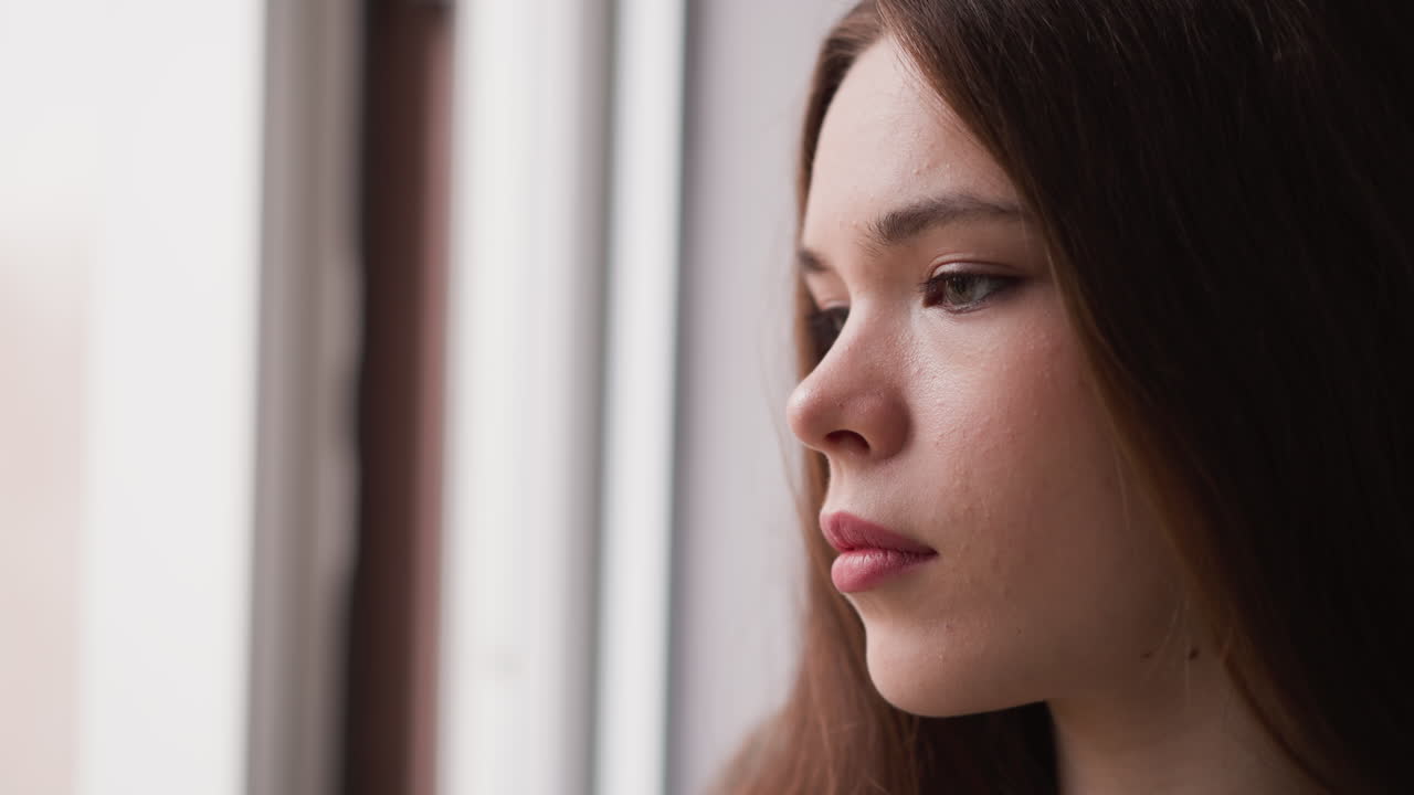 Distressed woman looks out of window closeup. Sorrowful lady deals with psychological trauma symptoms at home. Pensive mood expression by model
