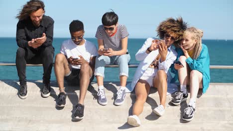 young diverse people with mobile phones on seafront