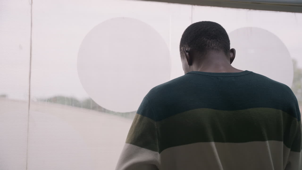 Urban man observes water scene. Silhouette of man looking at water through window view. Urban individual wearing striped clothing gazes contemplatively at reflective water scene beyond window