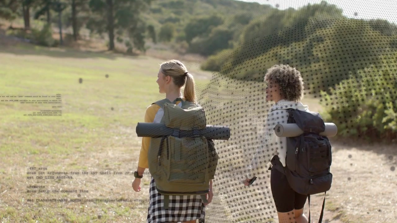 Sunlit meadow inviting two women carrying large backpacks and rolled mats, walking toward treeline