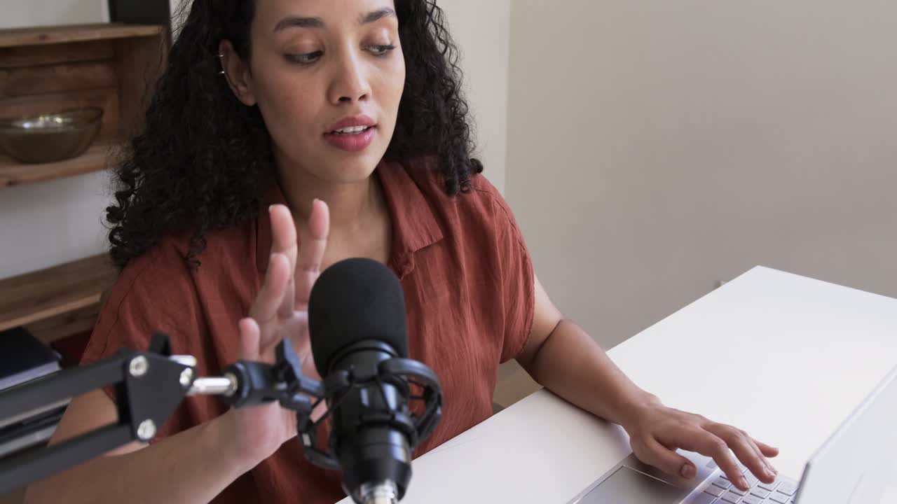 Femme afro-américaine en chemise de couleur rouille, s'arrêtant de taper, saisissant le micro, enregistrant de l'audio, vérifiant son ordinateur portable.