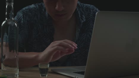close up de un hombre asiático bebiendo vodka mientras trabaja en una computadora portátil con fondo negro