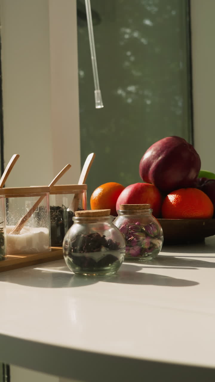 Tabletop hosts porcelain cup jars and fruits. Array of aromatic spices and dried herbs and assortment of nourishing fruits grace kitchen setting