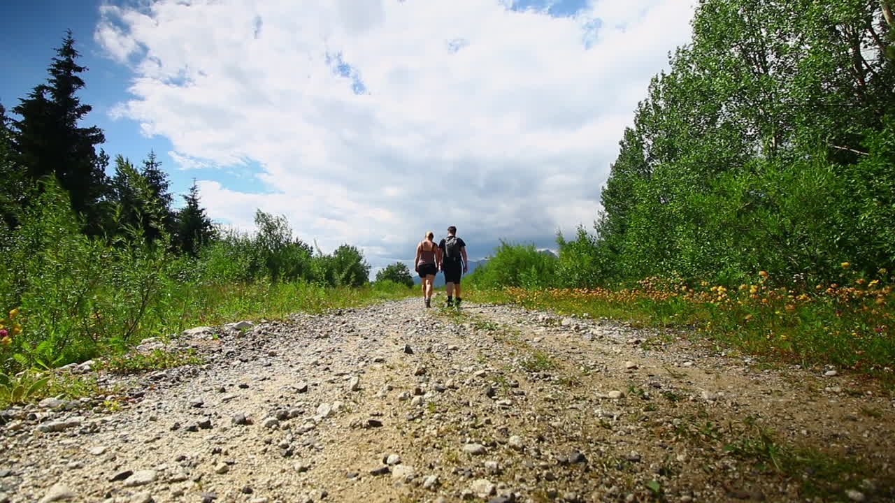 Man and woman, couple, walking away from camera, on hiking path in Poprad Slovakia during summer. Gravel path, blue skies wide shot.