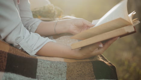 close-up of a lady hand with a bangle turning to a new page on a checkered blanket, enveloped in a golden glow that highlights the serene outdoor setting