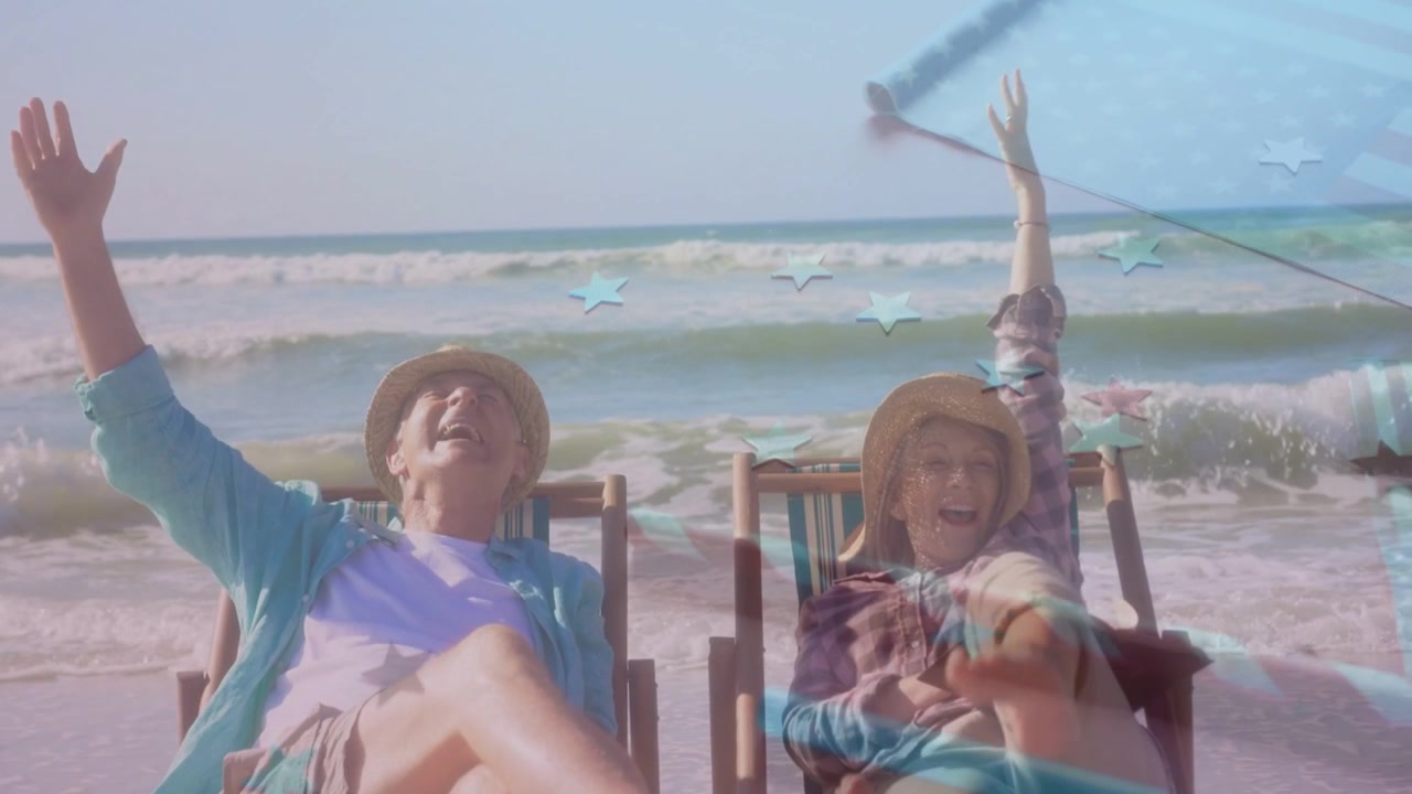 Pareja de ancianos en sillas de rayas junto a la playa, saludando y provocando una superposición de bandera de estrellas que marca el 4 de julio.