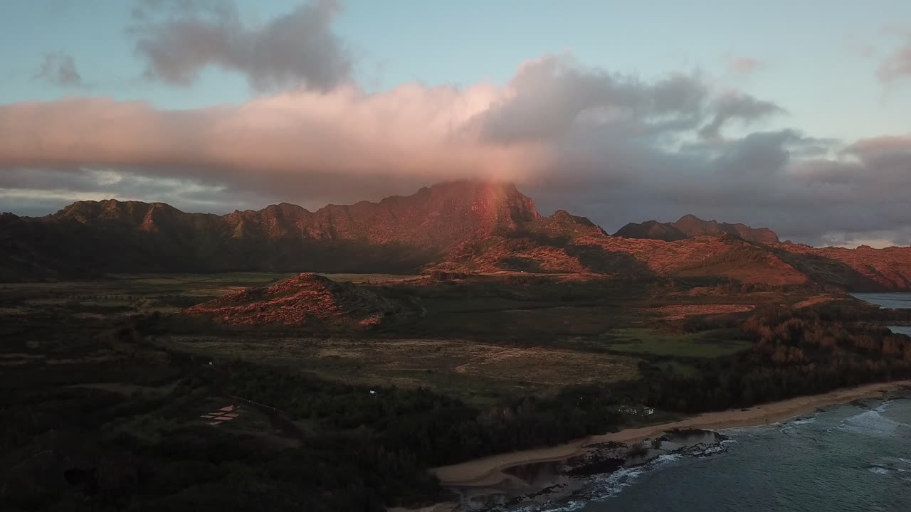 Drone flying down with mountain and rainbow at sunset above ocean in Kauai, Hawaii