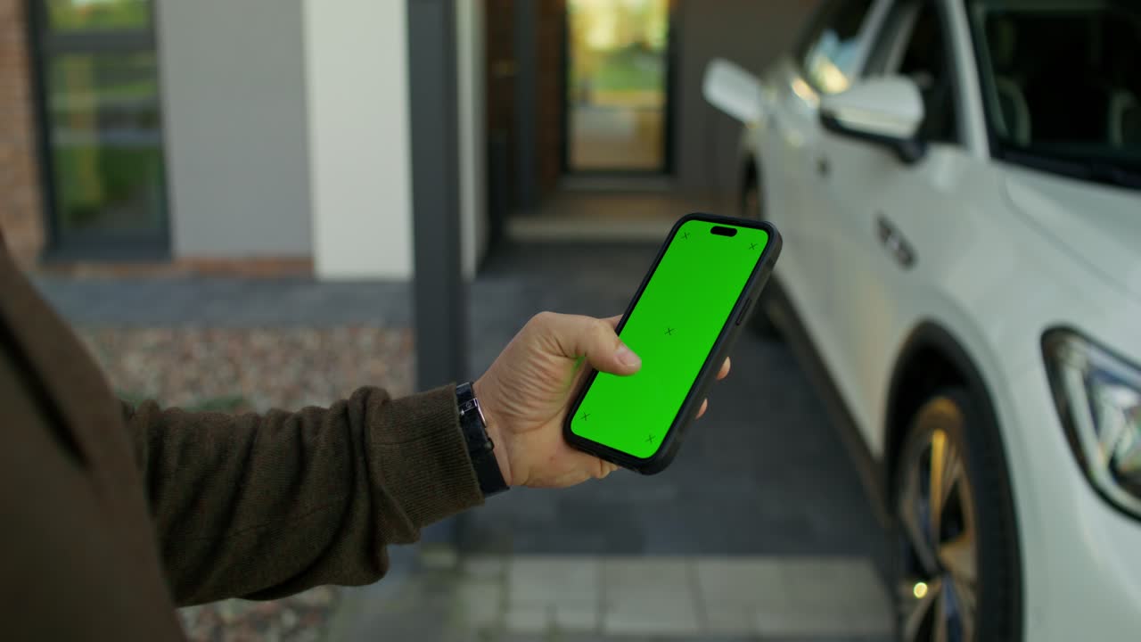 persona que utiliza un teléfono inteligente para cargar un vehículo eléctrico en casa