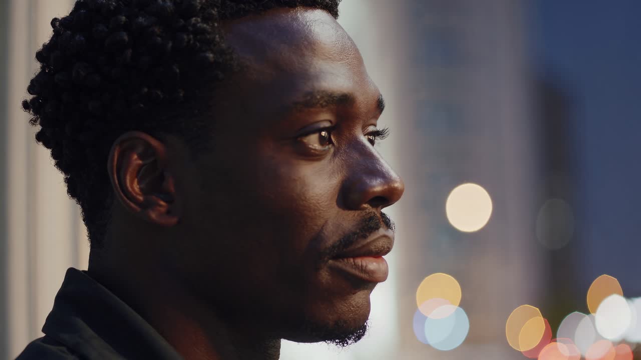 Close-up video shot of a man in profile, capturing thoughtful expression against a blurred cityscape