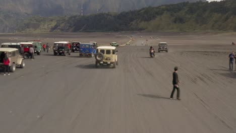 drone shot following several toyota land cruisers driving tourists in the sea of sand next to mount bromo, east java, indonesia