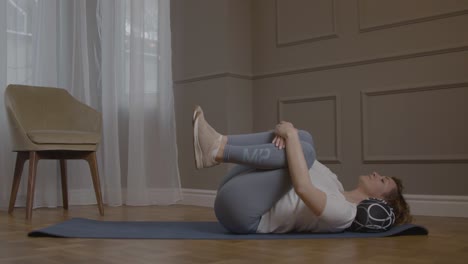 mujer caucásica en colchoneta de yoga levantando la pierna izquierda en el aire