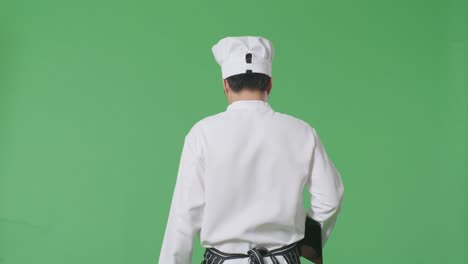 back view of asian man chef holding a tablet while walking in the green screen background studio