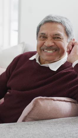 retrato de video vertical de un hombre bi-racial mayor feliz sentado en el sofá sonriendo a la cámara