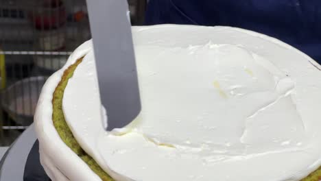 pastry chef using spatula to frost a smooth cake with buttercream meringue frosting while spinning the revolving cake turntable stand, close up shot in commercial kitchen bakery setting