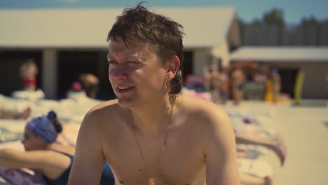 close-up young man is sitting on the beach on sun lounger looking for somebody with his eyes