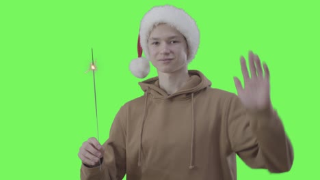 retrato de un adolescente caucásico con un sombrero de navidad sosteniendo una chispa. un niño feliz posando en el fondo verde. año nuevo, vacaciones, celebración, concepto de fiesta, chromakey.
