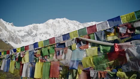 banderas de oración en las montañas nevadas de nepal, banderas de oración budistas tibetanas coloridas en el cielo azul en un día soleado en los himalayas en annapurna, banderas budistas coloridas en la naturaleza con montañas nevadas