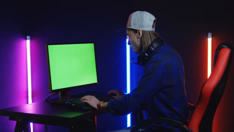 young man playing on the computer with chroma key screen in a room with colorful neon lamps on the wall