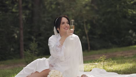 wedding bride in boudoir dress sitting in morning garden drinking champagne woman in night gown veil