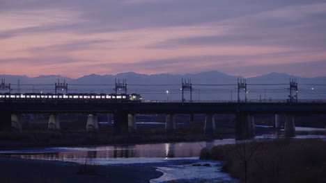 japanese train passing by futakotamagawa river with reflection on water during beautiful twilight in tokyo, japan