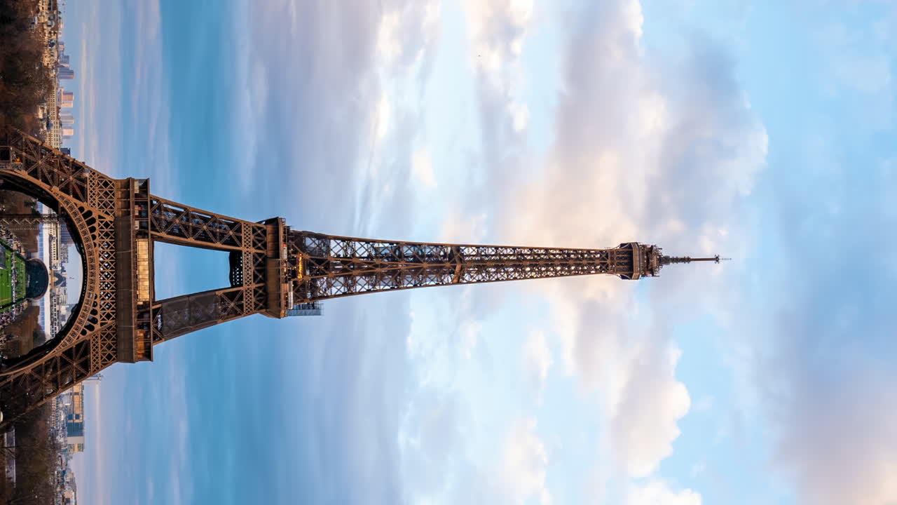 Paris, France - January 4, 2023: Cars and people moving on the street under the Eiffel Tower in Champ de Mars. Vertical