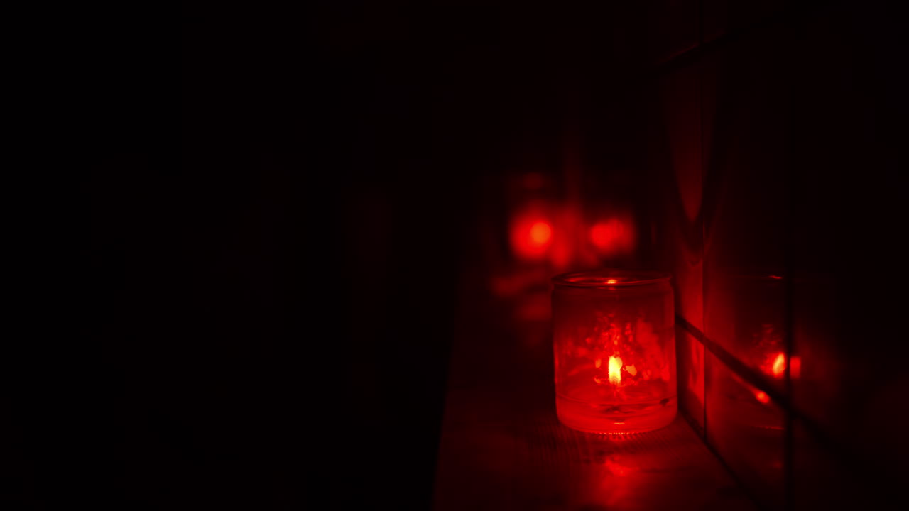 Vela roja en un tarro de cristal que proyecta un brillo cálido, reflejado en una superficie cercana. Ambiente de club oscuro
